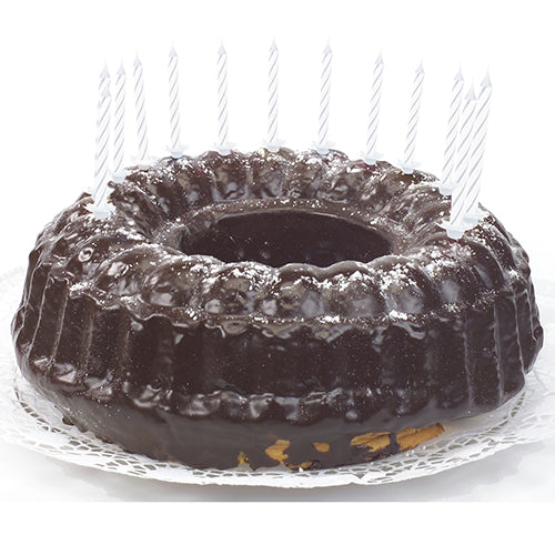 Um bolo de chocolate com cobertura brilhante, decorado com velas de aniversário PAPSTAR GmbH de 6 cm, brancas com suporte (24 unidades), distribuídas uniformemente na borda e colocadas sobre um toalhete de renda branco.