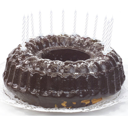 Um bolo de chocolate com cobertura brilhante, decorado com velas de aniversário PAPSTAR GmbH de 6 cm, brancas com suporte (24 unidades), distribuídas uniformemente na borda e colocadas sobre um toalhete de renda branco.