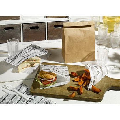 Uma mesa com um sanduíche, um hambúrguer e batatas fritas, embrulhados em PAPSTAR 5 papéis de embrulho 3 cm x 2 cm "Newsprint" da PAPSTAR GmbH, ao lado de um saco de papel pardo, copos e talheres de plástico, bem como uma tábua de servir de madeira sobre uma superfície branca.