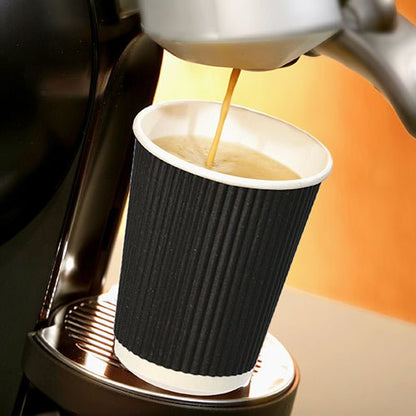 Um copo Starpak 25, Pappe "To Go" Ripple Wall está em uma bandeja de metal sob o bico de uma máquina de café, enquanto café quente é despejado, destacando-se contra um fundo suavemente iluminado e de tom quente.
