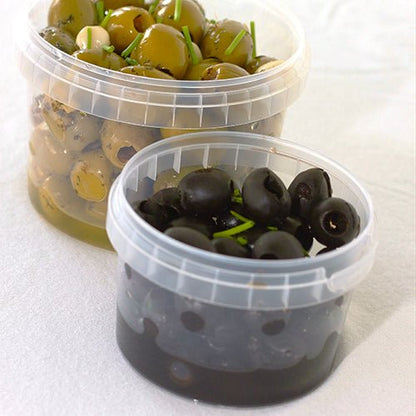 Em dois copos de delicatessen Starpak 30 transparentes (770 ml, PP, Ø 11,8 cm · 11,3 cm) com fecho de originalidade, azeitonas estão dispostas sobre um fundo branco - no copo traseiro azeitonas verdes com ervas e na frente azeitonas pretas com guarnição de ervas.