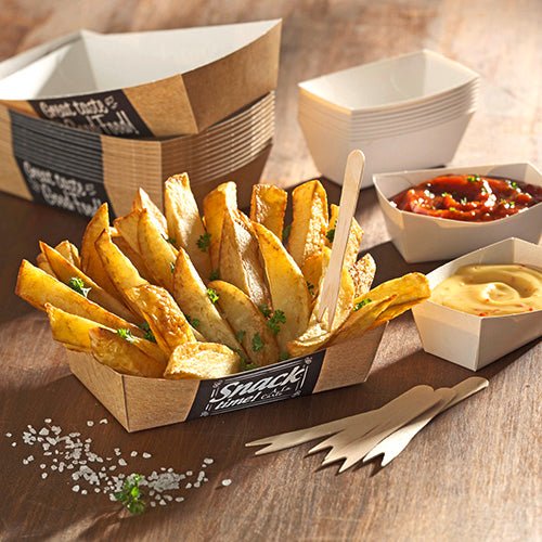 Uma PAPSTAR 50 embalagem de batatas fritas "pure" (3,5 x 7 cm) da PAPSTAR GmbH contém pedaços de batata grossos com salsa, além de dois molhos para mergulho, garfos adicionais, embalagens vazias e sal sobre a mesa de madeira para um toque ecológico.