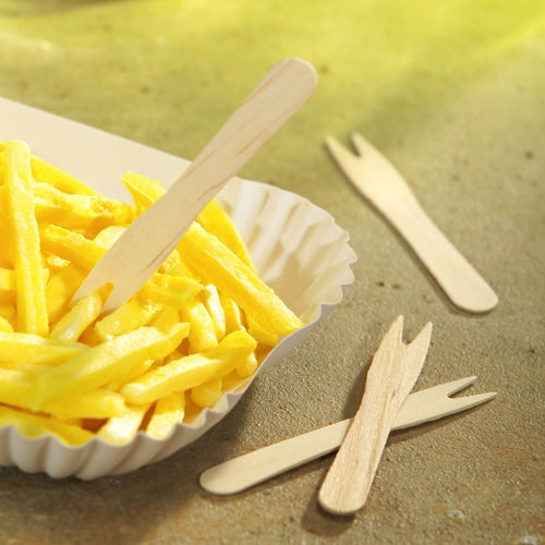 Auf einer weißen Papierschale mit Pommes frites liegt eine PAPSTAR Holz Pommes-Frites-Gabel; daneben liegen zwei weitere umweltfreundliche 8,5 cm Holzgabeln aus der 50er-Packung von PAPSTAR (pure, 50 Stück, PAPSTAR GmbH) und unterstreichen so den nachhaltigen Umgang mit Lebensmitteln.