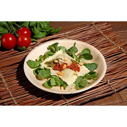 Um prato de ravioli com pesto, molho de tomate seco ao sol, pinhões e queijo é servido em um verde fresco em uma tigela de folha de palma PAPSTAR (17,5 cm), uma tigela ecológica do conjunto de 6 peças da PAPSTAR GmbH, com tomates e verduras ao fundo.