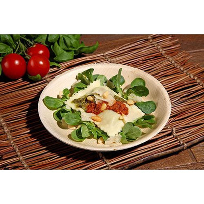 Um prato de ravioli com pesto, molho de tomate seco ao sol, pinhões e queijo é servido em um verde fresco em uma tigela de folha de palma PAPSTAR (17,5 cm), uma tigela ecológica do conjunto de 6 peças da PAPSTAR GmbH, com tomates e verduras ao fundo.