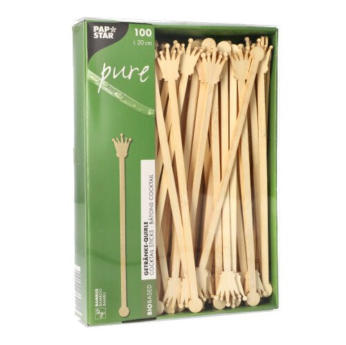 Um pacote com 100 PAPSTAR misturadores de bebidas de 20 cm feitos de bambu biodegradável, em forma de coroa, parcialmente visíveis através da janela. A embalagem ostenta o logotipo da PAPSTAR GmbH.