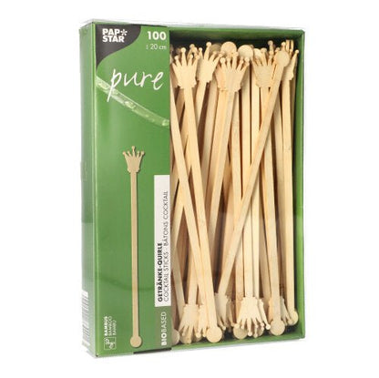 Um pacote com 100 PAPSTAR misturadores de bebidas de 20 cm feitos de bambu biodegradável, em forma de coroa, parcialmente visíveis através da janela. A embalagem ostenta o logotipo da PAPSTAR GmbH.