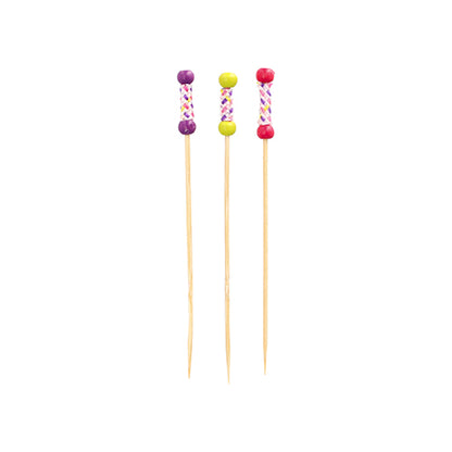 Três PAPSTAR 100 Fingerfood-Picker da PAPSTAR GmbH de bambu estão em pé. Cada palito tem uma alça decorativa com pérolas coloridas (roxa, amarela, rosa) e um padrão de cruz.