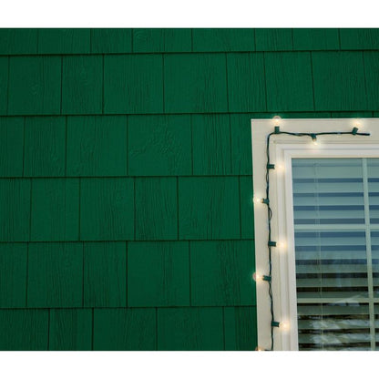 Uma imagem aproximada de uma parede de telhas verdes com uma janela emoldurada em branco do lado direito. Os clipes de luzes externas 3M Command™ (17017CLR-AWPU) fixam com segurança as luzes brancas ao redor da moldura, enquanto as persianas horizontais cobrem a janela.