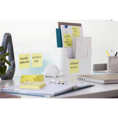 Uma mesa de escritório organizada com pastas, 3M Post-it® Super Sticky Z-Notes, Amarelo (76 mm x 76 mm), uma figura de tartaruga, uma planta, canetas, um laptop fechado e papéis. As notas nas pastas dizem "Avaliação de desempenho" e "Minimizar risco".