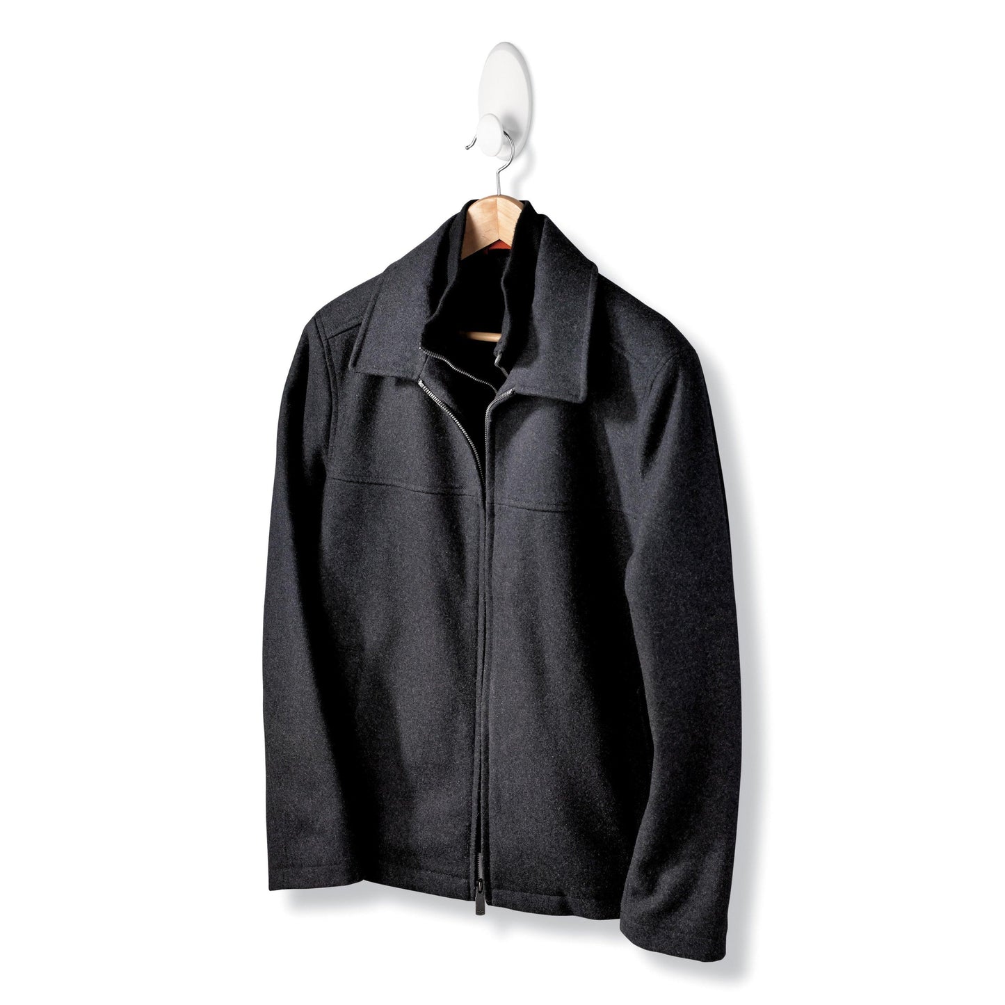 Eine schwarze Jacke mit Reißverschluss und Kragen hängt an einem Holzbügel des Command™ Kleider-Hakens, 17019-FGN, der eine Wandbefestigung ohne Bohren ermöglicht, vor einem schlichten weißen Hintergrund.