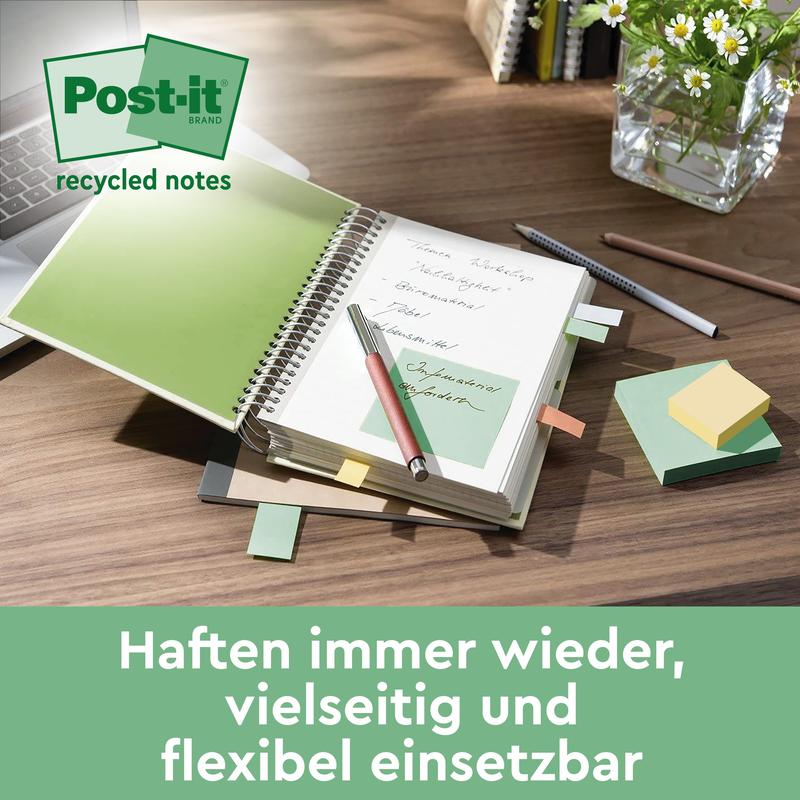 Uma mesa com um caderno aberto com Post-it® Super Sticky 100% Notas de Reciclagem (47,6 mm x 47,6 mm, 70 folhas/bloco, 100% PEFC) da 3M Deutschland GmbH, uma caneta esferográfica e lápis, clipes de papel e um vaso de vidro com folhas verdes. O texto em alemão aparece abaixo.