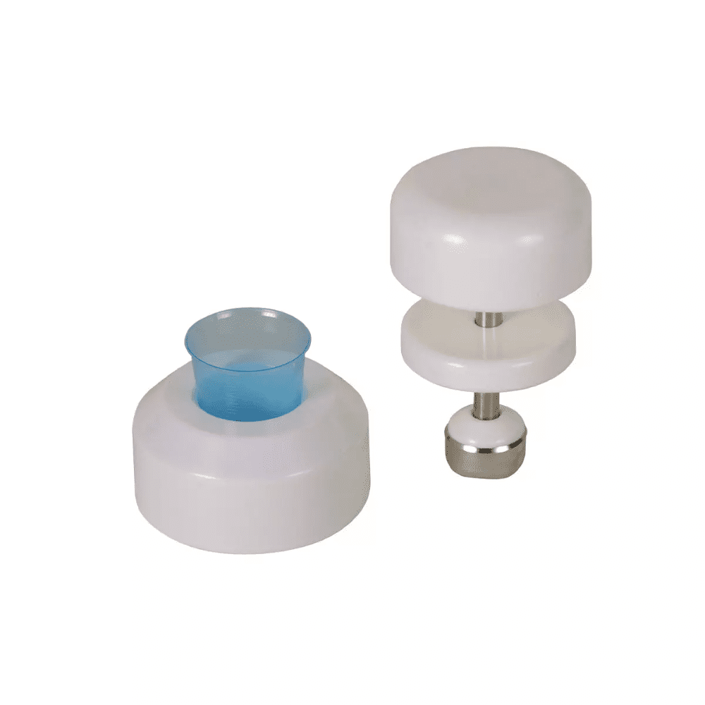 Em um fundo branco, são visíveis duas ferramentas de cozinha brancas de plástico. A ferramenta à esquerda tem uma forma cilíndrica com um inserto de plástico azul, enquanto a ferramenta à direita é um triturador de comprimidos AMPri para copos de medicação da AMPri Handelsgesellschaft mbH, que consiste em dois discos brancos conectados por uma haste de aço inoxidável com uma base de metal.