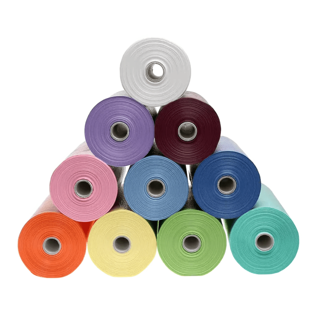Uma pilha em forma de pirâmide de dez rolos de babetes de paciente AMPri brilhantes em cores como branco, lilás, bordô, rosa, azul, azul-verde, laranja, amarelo, verde e prata com revestimento de PE da AMPri Handelsgesellschaft mbH brilha contra um fundo branco.