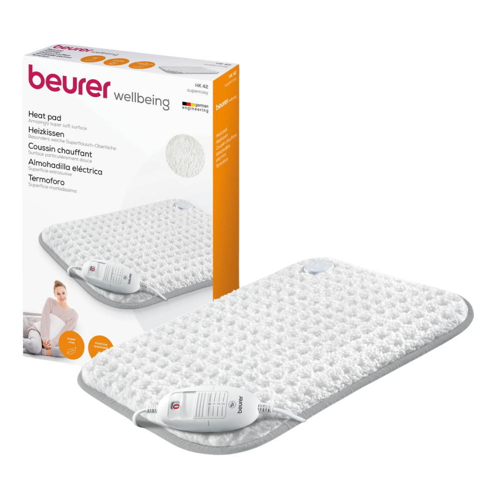Ao lado do produto está uma almofada térmica HK 42 Super-Cosy da Beurer GmbH com a marca "wellbeing" na embalagem. A almofada branca com borda cinza está equipada com um controlo remoto. A embalagem também mostra uma imagem da almofada térmica em uso e destaca a função de aquecimento rápido.