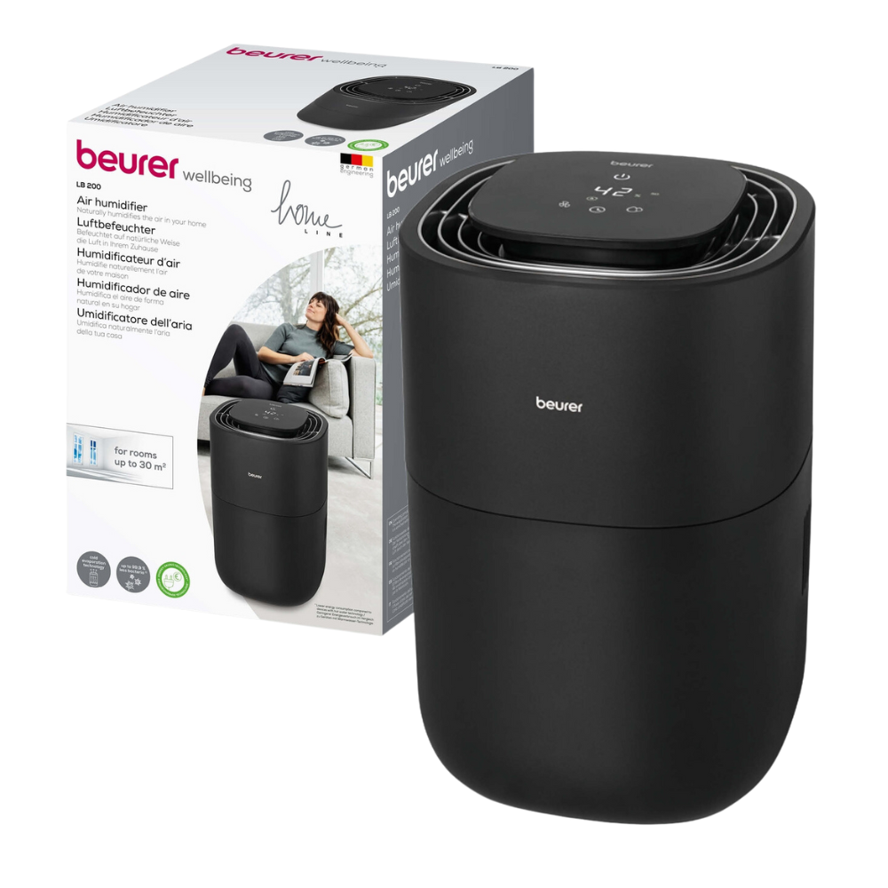 Um humidificador preto Beurer LB 200 da Beurer GmbH é colocado ao lado de sua caixa de embalagem, que além do nome da marca também contém uma imagem do humidificador e um texto multilíngue que diz que é adequado para salas de até 20 metros quadrados. Na imagem na caixa, vê-se uma mulher.
