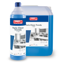 Uma garrafa e uma embalagem grande do detergente neutro e limpador de plástico Buzil Vario Clean Trendy T 560 da BUZIL-WERK Wagner GmbH & Co. KG prometem um efeito Easy-to-clean. A garrafa com a promessa de brilho sem manchas está posicionada em frente à embalagem, ambas estão adesivadas com uma imagem de uma turma de escola. O líquido no interior brilha azul.