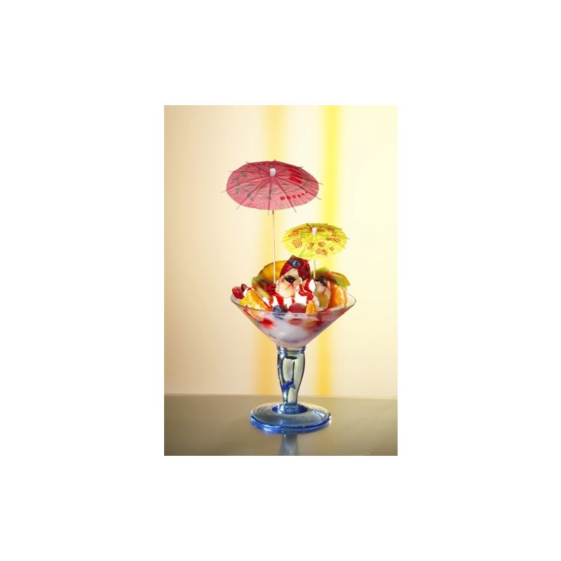 Em um copo de vidro há uma taça de sorvete colorida, decorada com bolas de cerejas, frutas cortadas e PAPSTAR Decorações sortidas da PAPSTAR GmbH. O fundo suavemente iluminado destaca a sobremesa de forma ideal.