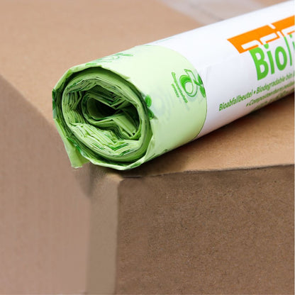 Um rolo de sacos de lixo biológico DEISS verde-claro de 30 litros, 06030, que são 100% compostáveis, está sobre uma caixa de cartão castanha. A embalagem está parcialmente visível e mostra um logotipo ecológico e a inscrição "Bio" em letras laranja em negrito da EMIL DEISS KG (GmbH + Co.).