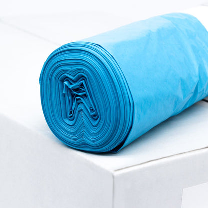 Um rolo de sacos de lixo azuis DEISS LDPE Tipo 60, 20772, 70 litros da EMIL DEISS KG (GmbH + Co.) está sobre uma caixa branca. Estes sacos duráveis, conhecidos por sua resistência ao rasgo, estão cuidadosamente enrolados para mostrar a estrutura em camadas do material reciclado. O fundo permanece simples e minimalista.