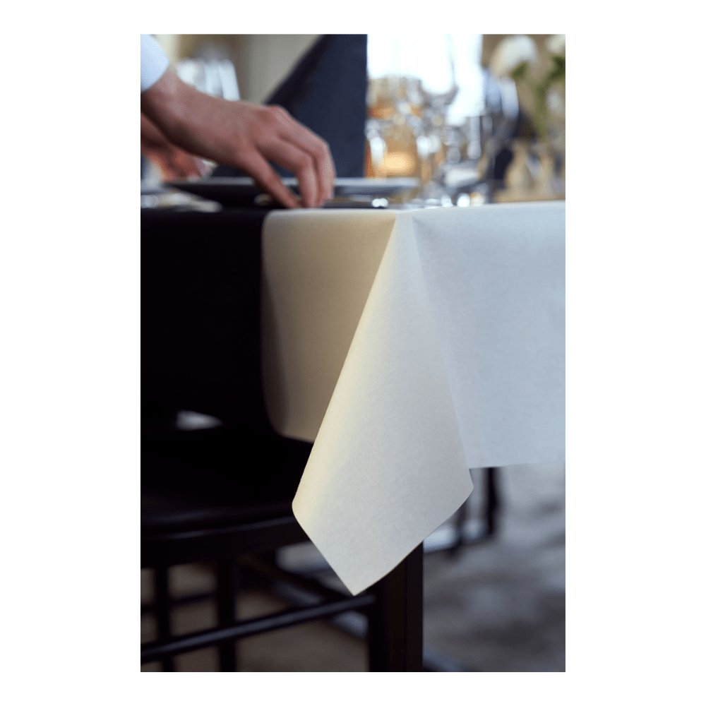 Uma pessoa ajusta uma toalha de mesa Duni Dunicel da Duni GmbH cuidadosamente dobrada em uma mesa posta com vidraria e um guardanapo preto dobrado, sugerindo uma disposição de mesa sofisticada.