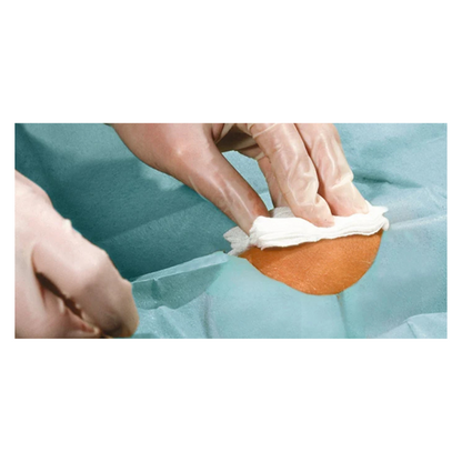 Um close-up de mãos enluvadas limpando uma pequena área de pele com um pano branco, cercado por panos Hartmann Foliodrape® Protect Lochtücher, autoadesivo, estéril, embalado individualmente, da Paul Hartmann AG.