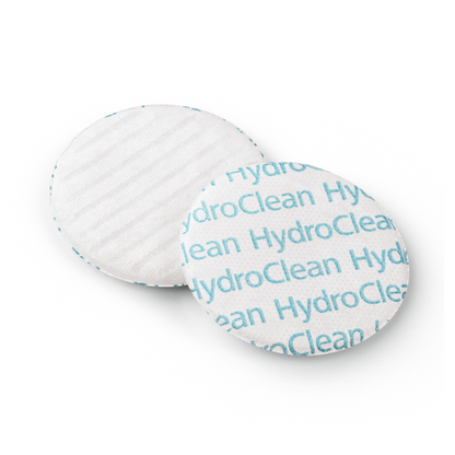 Dois discos de algodão redondos sobre fundo branco, um disco mostra para cima o padrão de texto "Paul Hartmann AG HydroClean® Wundauflage" em azul, o outro disco mostra para baixo uma superfície lisa.