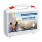 Uma caixa de primeiros socorros Holthaus Nautisave® branca com detalhes vermelhos, rotulada com "Holthaus Medical NAUTISAVE Primeiros Socorros a Bordo / First Aid". A frente da mochila mostra uma imagem de duas pessoas em um veleiro ao pôr do sol, sendo assim ideal para ambientes marítimos.