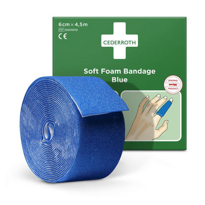 Em frente a uma caixa de embalagem verde, é apresentada uma rolo de dispensador de penso azul Holthaus Soft Foam Bandage com a inscrição 6 cm x 4,5 m. A caixa mostra uma mão com o penso enrolado em torno de um dedo e exibe a inscrição "Cederroth Soft Foam Bandage Azul". Este produto encaixa-se perfeitamente no rolo de recarga de espuma suave da Holthaus Medical GmbH & Co. KG.