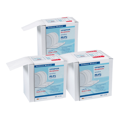 Três caixas de pensos Holthaus Ypsipor, pensos de tecido não tecido da Holthaus Medical GmbH & Co. KG são exibidas sobre um fundo branco. Cada caixa contém 18 peças de pensos de tecido não tecido amigáveis para a pele, com as dimensões de 6 cm x 5 m. A embalagem predominantemente branca apresenta acentos azuis e vermelhos e é perfeita para artigos de primeiros socorros.