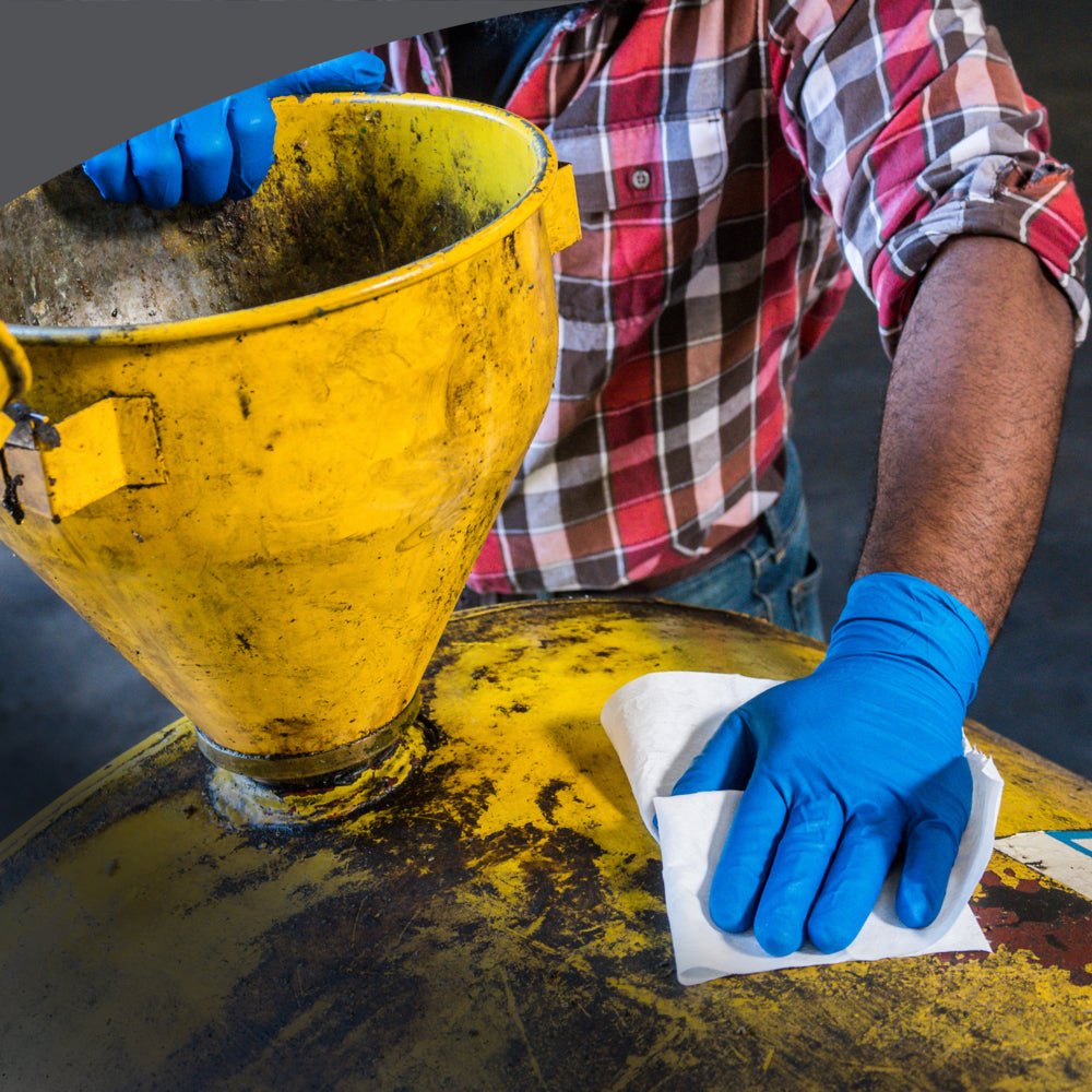 Uma pessoa com luvas azuis e uma camisa xadrez limpa um contentor industrial amarelo, utilizado para limpeza industrial, com um pano dobrado em quarto WypAll® X80 PowerClean da Kimberly-Clark GmbH. O contentor tem um grande funil na parte superior.