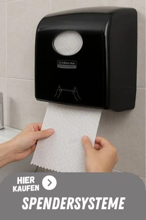 Person zieht ein Papiertuch aus einem schwarzen Wandspender in einem Waschraum, unten im Bild steht der Schriftzug ‚Hier kaufen – Spendersysteme'.