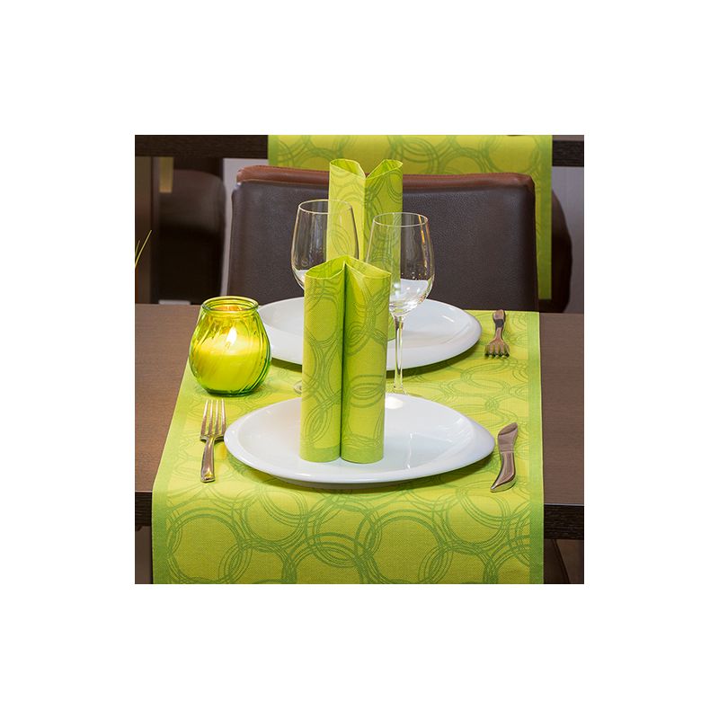 Uma mesa de jantar está elegantemente posta para duas pessoas com pratos brancos, copos de haste e talheres. Guardanapos verdes são artisticamente colocados nos pratos. Um castiçal verde está sobre um corredor de mesa PAPSTAR semelhante a tecido PV-Tissue Mix "Coleção ROYAL" da PAPSTAR GmbH, cujo padrão circular adiciona sofisticação à cena.