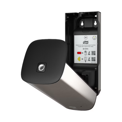 O dispensador de cuidados da pele Tork 460009 da TORK – Essity Professional Hygiene Germany GmbH é apresentado abertamente e possui um design moderno e elegante com superfície metálica e painel frontal preto. No interior, estão visíveis manuais de instruções e códigos QR. Este dispensador de parede em aço inoxidável é projetado para uma utilização eficiente de toalhas e possui uma inovadora tecnologia de sensor de intuição.