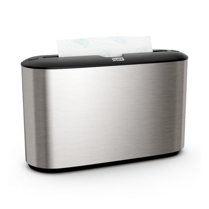 O dispensador de mesa Tork Xpress® 460005 para toalhas de mão Multifold da Essity Professional Hygiene Germany GmbH destaca-se pelo seu design em aço inoxidável sofisticado. O seu exterior prateado é acentuado por uma parte superior preta, com uma seção de toalhas de papel brancas elegantemente projetando-se da ranhura superior. Ideal para utilizadores de toalhas de mão Multifold que apreciam tanto estilo como funcionalidade.
