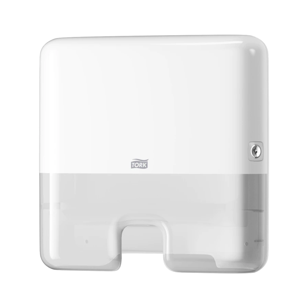 Um Tork Xpress® 552100 Mini Dispensador para Toalhas Multifold Elevation H2, fabricado pela TORK – Essity Professional Hygiene Germany GmbH, está montado na parede. Possui um design retangular simples com bordas arredondadas, uma fechadura visível no lado direito e uma abertura na parte inferior para a distribuição de folhas únicas de toalhas multifold.