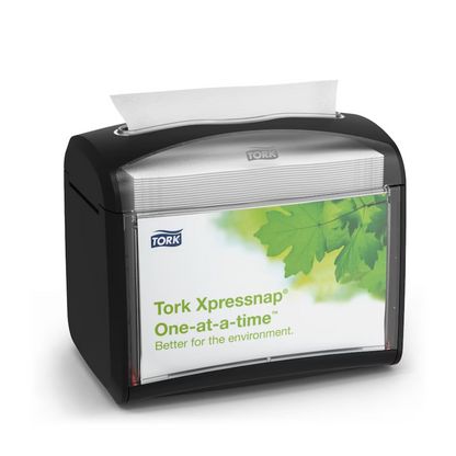 Um dispensador de mesa preto Tork Xpressnap® 272611 para guardanapos, distribuído pela TORK – Essity Professional Hygiene Germany GmbH, é apresentado com uma etiqueta com folhas verdes e a mensagem "Individualmente. Melhor para o ambiente". Um único guardanapo é parcialmente dispensado de cima para promover a higiene e um consumo eficiente de guardanapos.