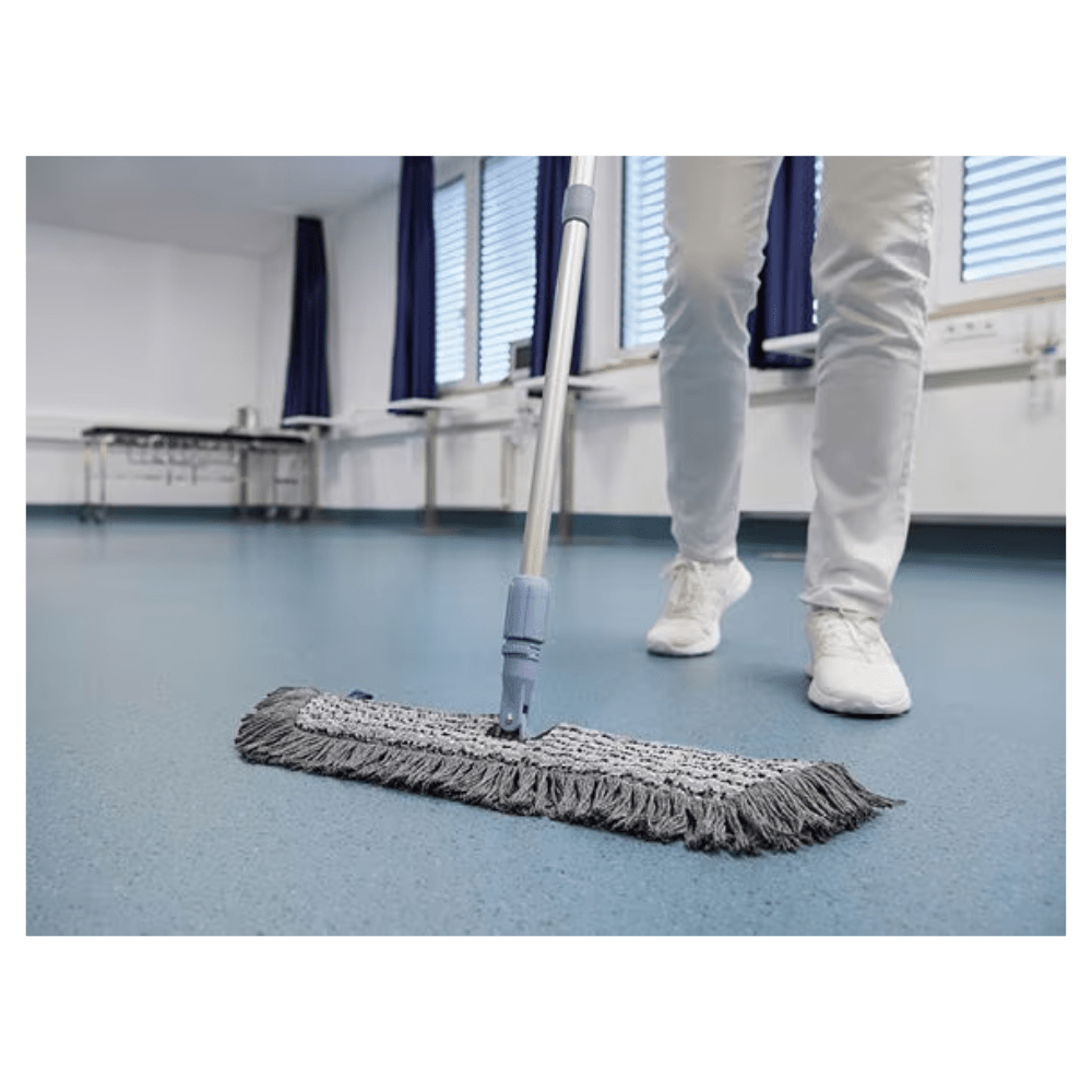 Uma pessoa de sapatos e calças brancos está a limpar um chão azul com um Vileda GmbH Professional Swep Duo r-MicroCombi Mop - 50 cm numa sala com persianas fechadas e cortinas azuis. Perto dali, há uma mesa dobrável e um aquecedor embaixo das janelas.