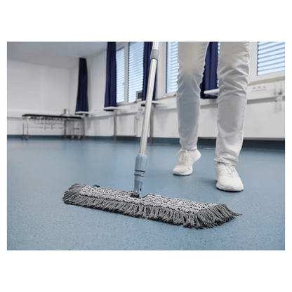 Uma pessoa de sapatos e calças brancos está a limpar um chão azul com um Vileda GmbH Professional Swep Duo r-MicroCombi Mop - 50 cm numa sala com persianas fechadas e cortinas azuis. Perto dali, há uma mesa dobrável e um aquecedor embaixo das janelas.
