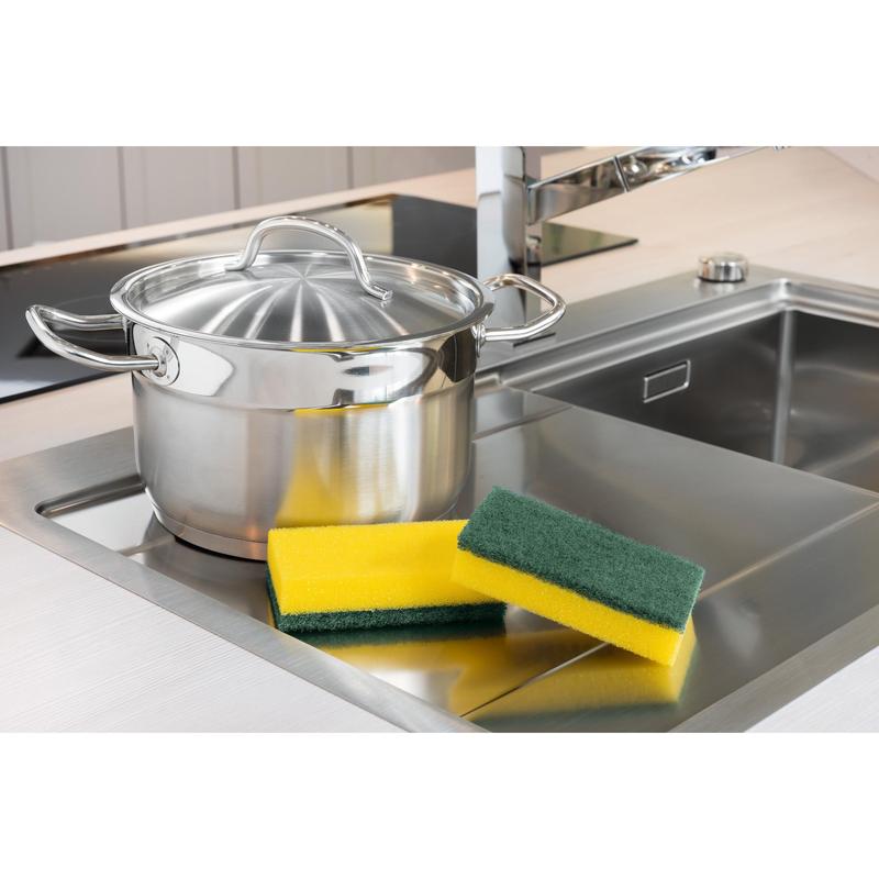 Uma panela de aço inoxidável com tampa está ao lado da pia. Ao lado estão três esponjas, incluindo uma esponja de limpeza Scotch-Brite® Classic XXL da 3M Deutschland GmbH (6 unidades por embalagem). Ao fundo, vê-se uma torneira moderna.