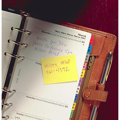 Um planejador encadernado em couro aberto mostra notas manuscritas de quinta-feira: "Almoço 13h John", "Conferência de imprensa 17h Hilton Hotel". Em um bloco amarelo de Post-it® Recycling Notes da 3M Deutschland GmbH está escrito: "Hilton Hotel 761-4392". As divisórias estão visíveis.