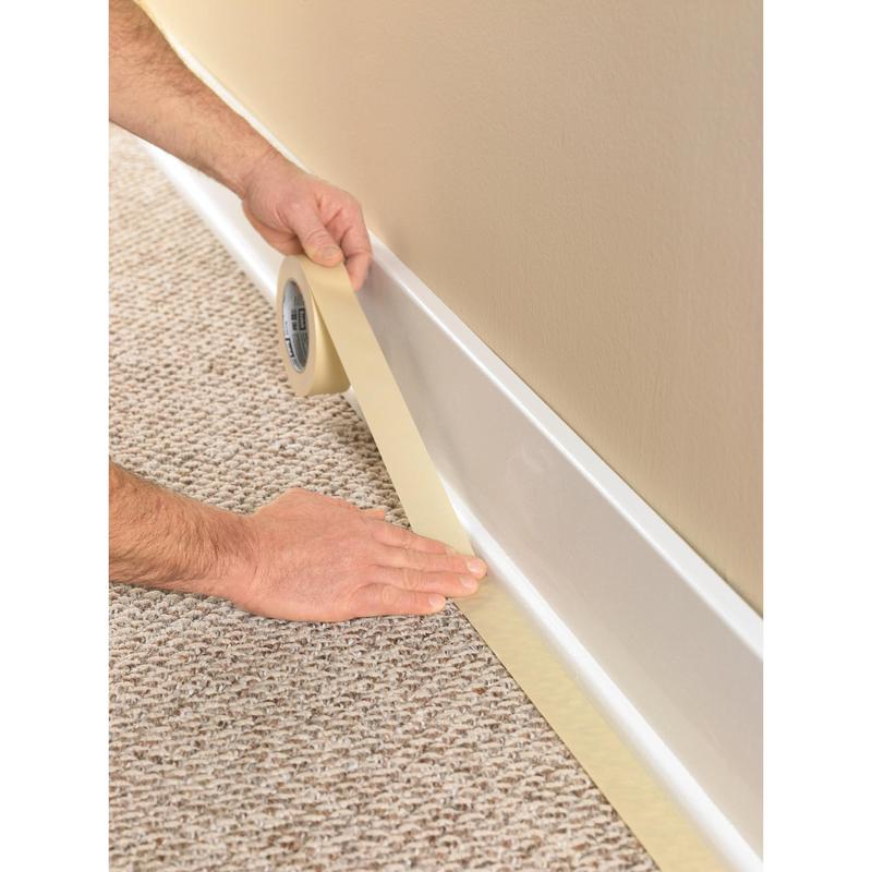 Uma pessoa usa a fita adesiva Scotch® Classic, 24 mm x 50 m (70% PEFC) da 3M Deutschland GmbH, para cobrir o rodapé onde o carpete encontra a parede, protegendo o revestimento durante trabalhos de pintura e renovação.