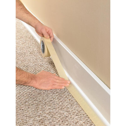 Uma pessoa usa a fita adesiva Scotch® Classic, 24 mm x 50 m (70% PEFC) da 3M Deutschland GmbH, para cobrir o rodapé onde o carpete encontra a parede, protegendo o revestimento durante trabalhos de pintura e renovação.