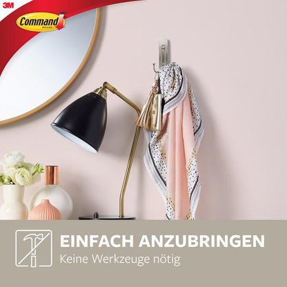 Um cachecol e um chaveiro pendem de um grande Command™ gancho duplo em níquel escovado (17036, 1 gancho, 1 tira) da 3M Deutschland GmbH, montado em uma parede rosa sobre lâmpada e vasos. Logotipo no canto superior esquerdo. Texto: "Fácil de aplicar. Sem necessidade de ferramentas.