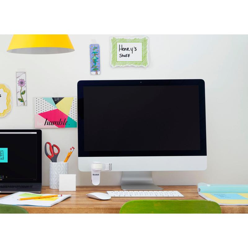 Uma mesa organizada com um grande monitor, um laptop fechado, um copo com canetas e tesouras, material de escritório e o dispensador de fita adesiva 3M Scotch™ Clip & Twist C19 com fita adesiva invisível Magic™ em exibição. Na parede, há notas decorativas como "Henry's Stuff".